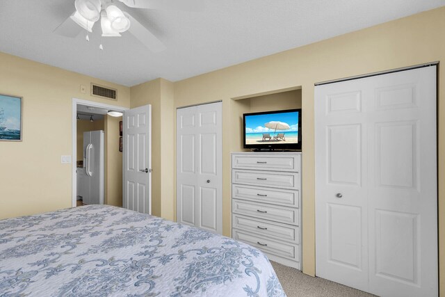 carpeted bedroom with freestanding refrigerator, visible vents, ceiling fan, and two closets