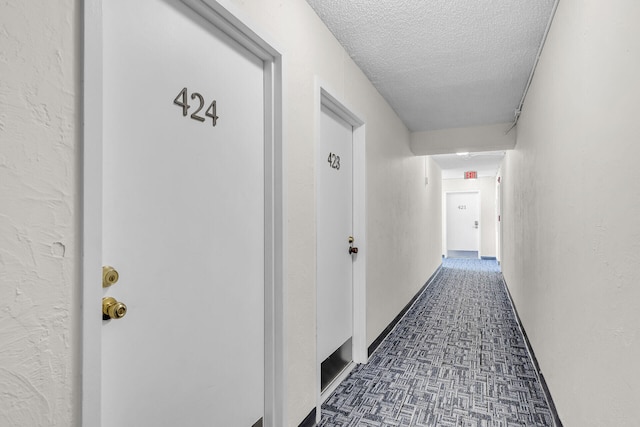 hall featuring a textured wall, dark carpet, and a textured ceiling