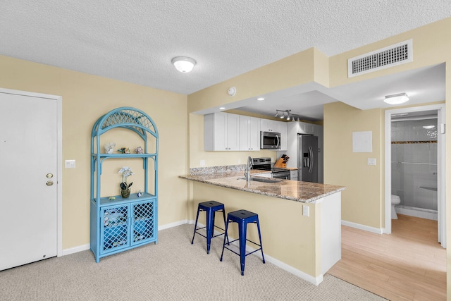 kitchen featuring stainless steel appliances, visible vents, white cabinets, a peninsula, and a kitchen bar