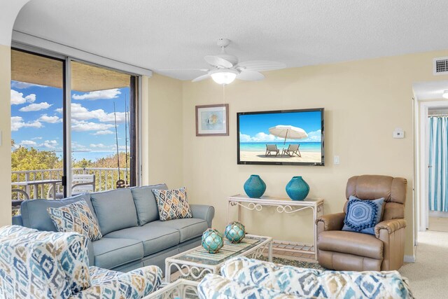 carpeted living area with a ceiling fan, visible vents, floor to ceiling windows, and a textured ceiling