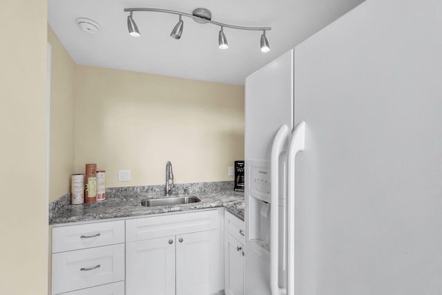 kitchen featuring stone countertops, white cabinets, rail lighting, white fridge with ice dispenser, and a sink