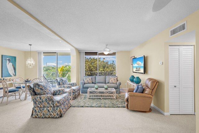 living room with a textured ceiling, ceiling fan with notable chandelier, carpet floors, visible vents, and baseboards