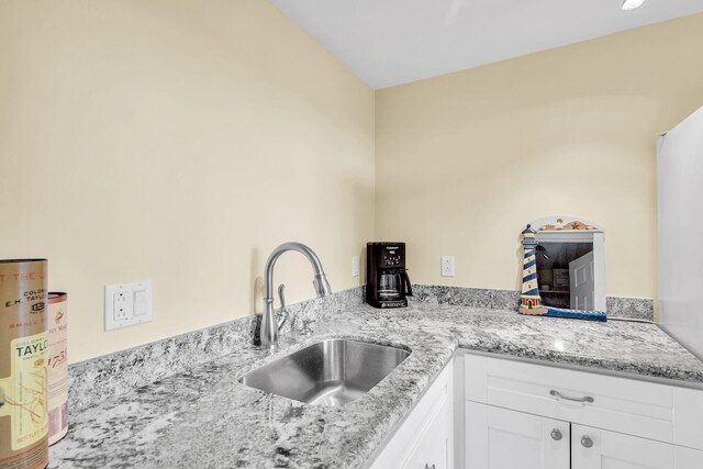 kitchen with light stone counters, gas water heater, white cabinets, and a sink