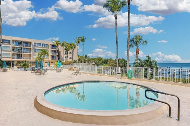 pool featuring a patio area, a water view, and fence