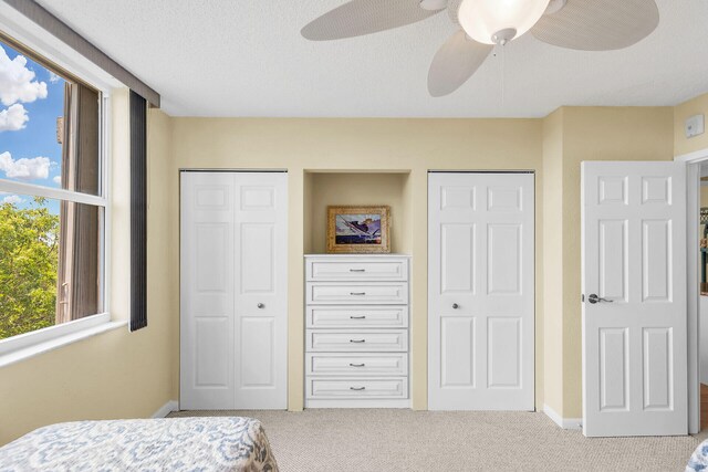 carpeted bedroom featuring multiple closets, a textured ceiling, baseboards, and a ceiling fan