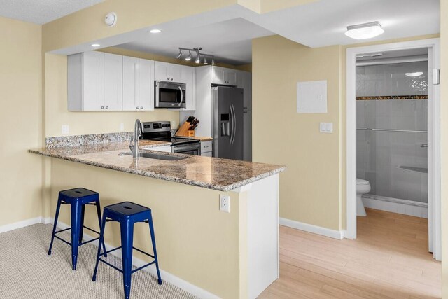 kitchen featuring white cabinets, appliances with stainless steel finishes, a breakfast bar, a peninsula, and light stone countertops