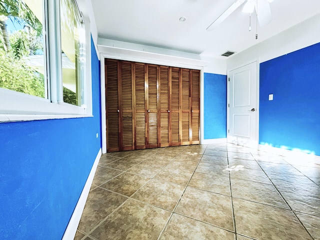 unfurnished bedroom with a closet, baseboards, tile patterned floors, a ceiling fan, and visible vents