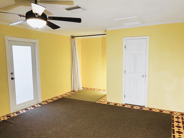 spare room featuring ceiling fan, carpet, ornamental molding, visible vents, and attic access