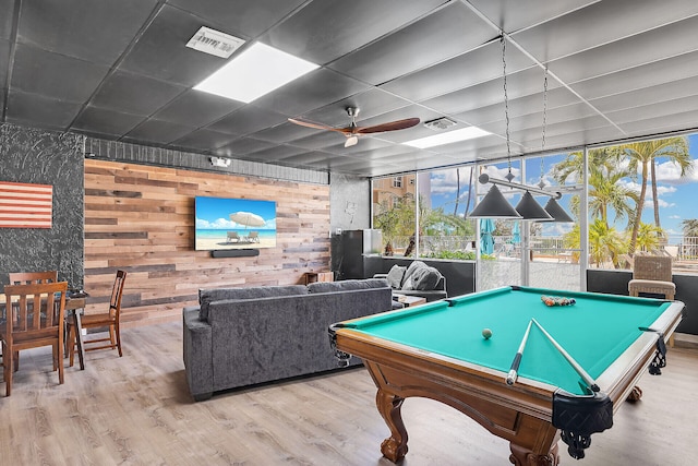 rec room with ceiling fan, a healthy amount of sunlight, light wood-type flooring, and wood walls