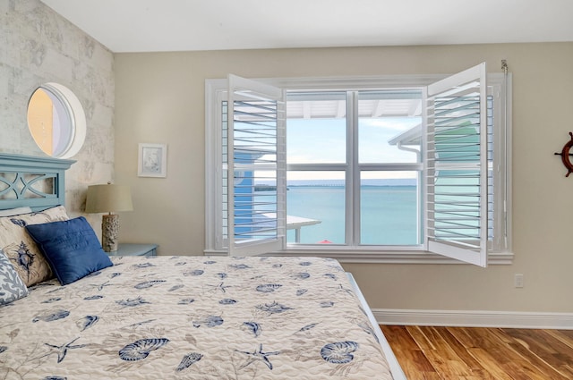 bedroom with hardwood / wood-style floors and a water view