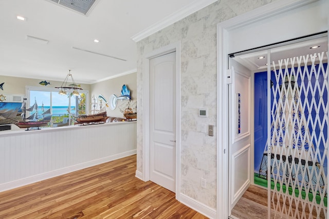 hall with a notable chandelier, crown molding, wood-type flooring, and elevator