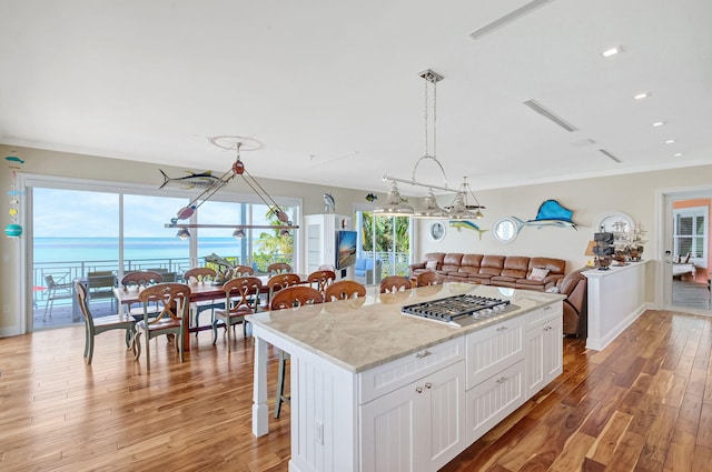 kitchen with stainless steel gas cooktop, a water view, hanging light fixtures, a kitchen island, and white cabinets