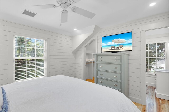bedroom with multiple windows, light wood finished floors, wooden walls, ceiling fan, and recessed lighting