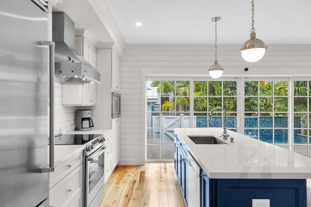 kitchen featuring built in appliances, a sink, wall chimney exhaust hood, light wood finished floors, and a kitchen island with sink
