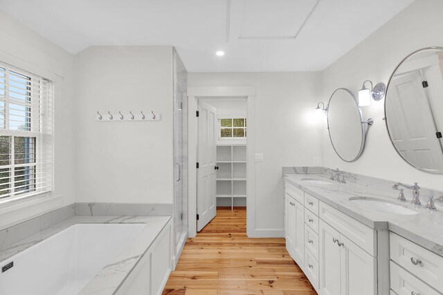 bathroom featuring wood finished floors, double vanity, a bath, recessed lighting, and a stall shower