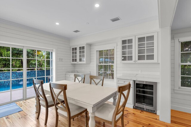 dining area with wine cooler, light wood-style floors, recessed lighting, and wood walls