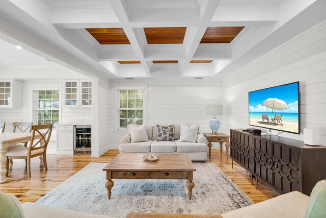 living room with beverage cooler, light wood-type flooring, healthy amount of natural light, beam ceiling, and coffered ceiling