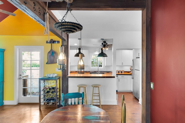 kitchen with wood finished floors, freestanding refrigerator, a peninsula, white cabinetry, and beam ceiling