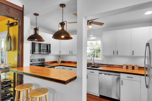 kitchen featuring butcher block counters, appliances with stainless steel finishes, white cabinetry, a sink, and a kitchen breakfast bar