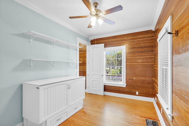 unfurnished room featuring ornamental molding, ceiling fan, light wood-type flooring, and wood walls