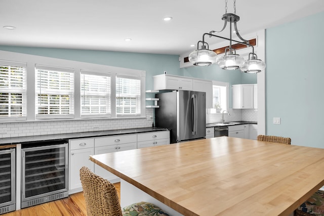 kitchen featuring butcher block countertops, stainless steel appliances, white cabinets, decorative light fixtures, and beverage cooler