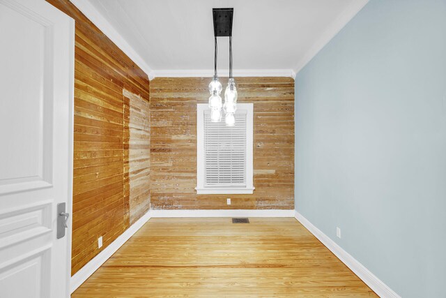 unfurnished dining area with crown molding, hardwood / wood-style flooring, and wood walls