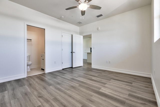 unfurnished bedroom with baseboards, ensuite bathroom, wood finished floors, and visible vents