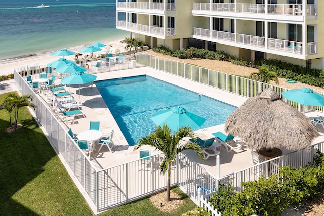 pool featuring a water view, fence, a patio area, and a view of the beach