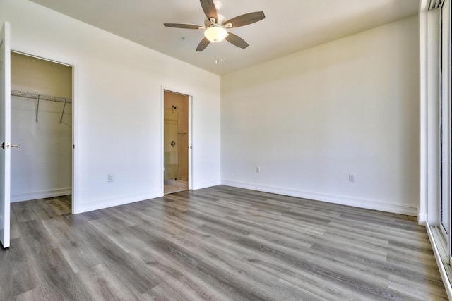 unfurnished bedroom with a walk in closet, wood finished floors, baseboards, a closet, and ensuite bathroom