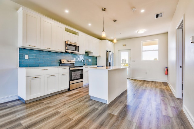 kitchen with appliances with stainless steel finishes, light wood-style floors, decorative backsplash, a kitchen island, and visible vents