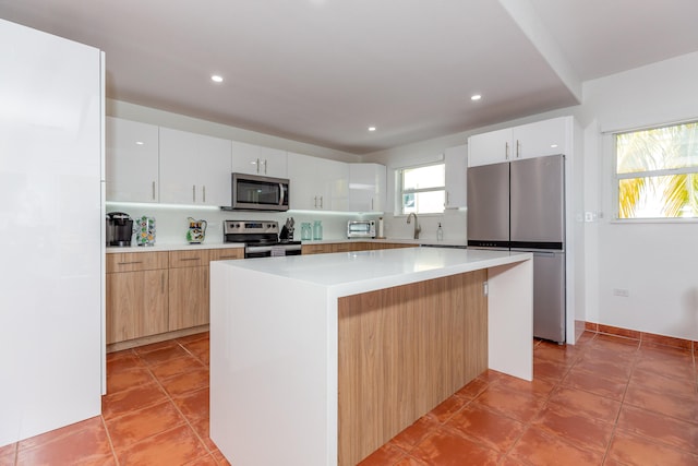 kitchen featuring sink, white cabinetry, a kitchen island, stainless steel appliances, and light tile patterned flooring