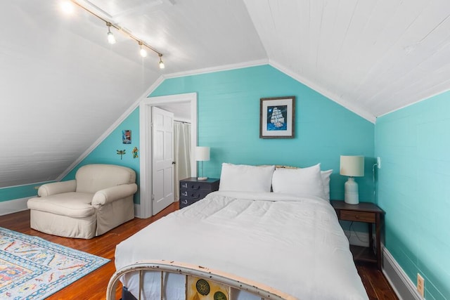 bedroom with vaulted ceiling, rail lighting, dark wood-type flooring, and ornamental molding