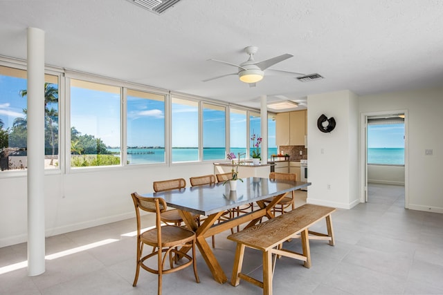 dining space with a water view, ceiling fan, a view of the beach, and a textured ceiling