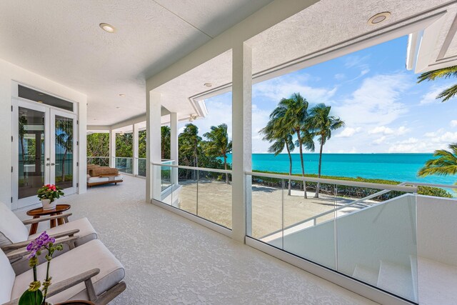 sunroom featuring a water view, a view of the beach, and french doors