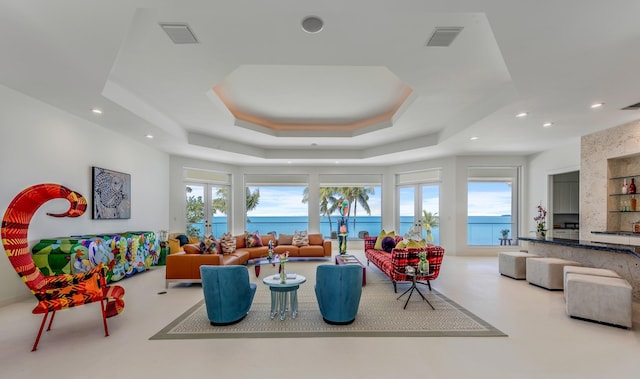 living room with french doors, a water view, plenty of natural light, and a tray ceiling