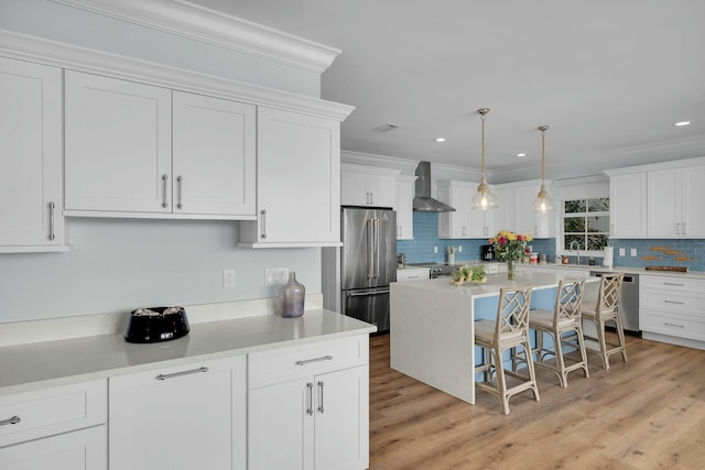kitchen with pendant lighting, light countertops, appliances with stainless steel finishes, white cabinetry, and wall chimney range hood