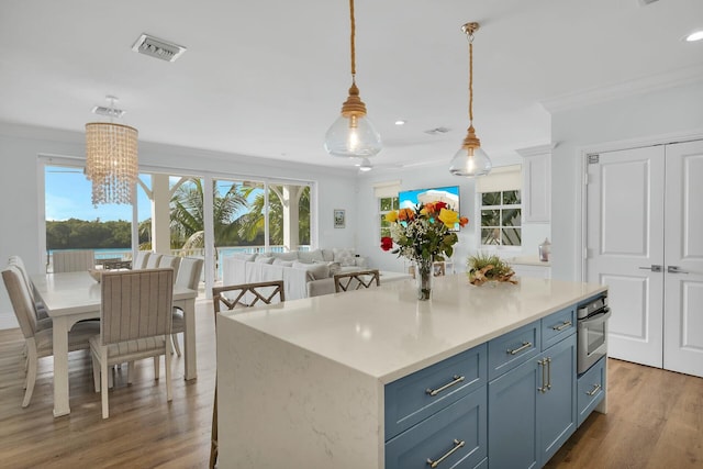 kitchen with visible vents, ornamental molding, a center island, light countertops, and pendant lighting