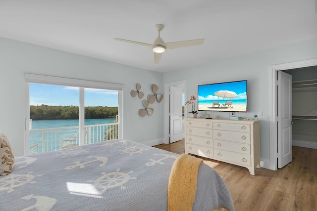 bedroom featuring light wood-style floors, a water view, a walk in closet, and access to exterior