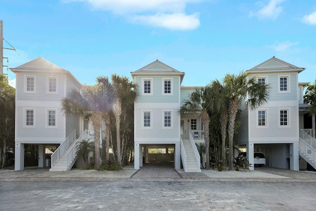 coastal home featuring a carport, decorative driveway, and stairs
