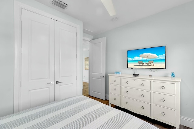 bedroom with baseboards, visible vents, dark wood-style flooring, and a closet