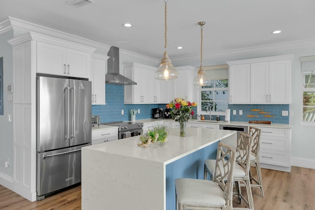 kitchen with white cabinetry, light countertops, appliances with stainless steel finishes, wall chimney range hood, and a center island