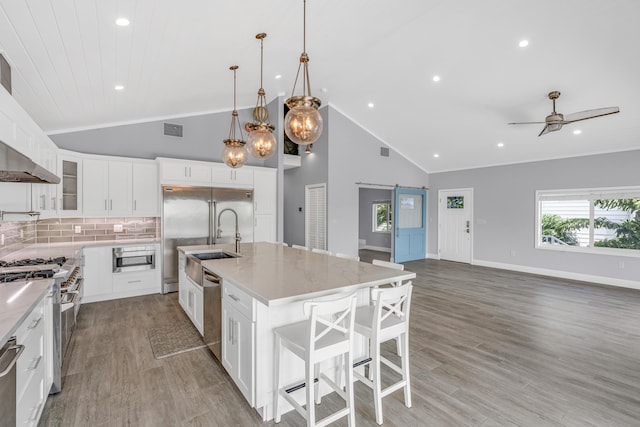 kitchen featuring white cabinetry, decorative light fixtures, a center island with sink, high quality appliances, and a barn door