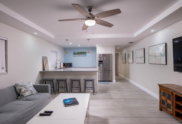 living room with sink, a tray ceiling, light hardwood / wood-style flooring, and ceiling fan