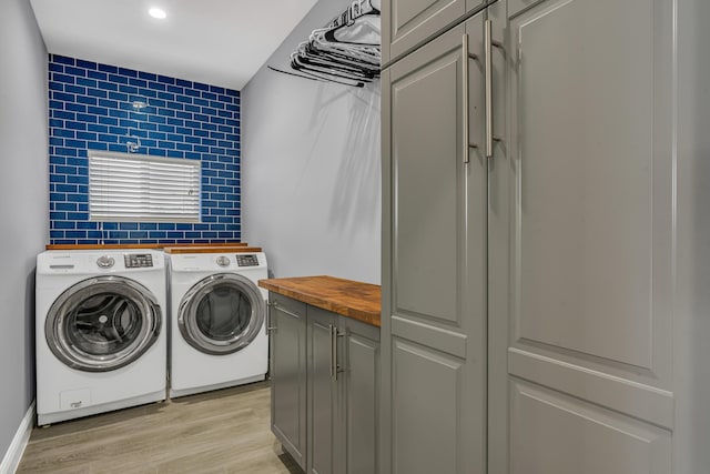 clothes washing area featuring cabinets, washer and clothes dryer, and light hardwood / wood-style flooring