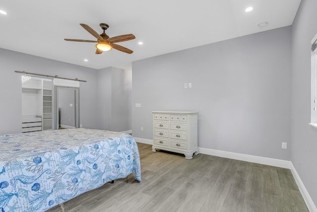 bedroom with a barn door, ceiling fan, and light wood-type flooring