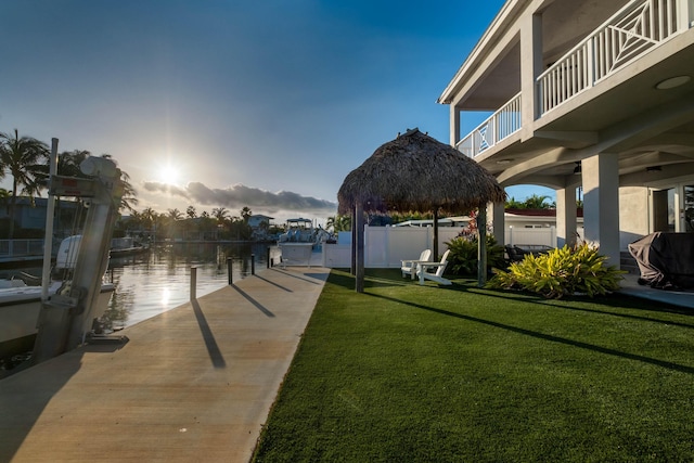 yard at dusk featuring a gazebo, a water view, a boat dock, and a balcony