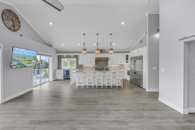 kitchen featuring a breakfast bar area, built in refrigerator, white cabinetry, a center island, and decorative light fixtures