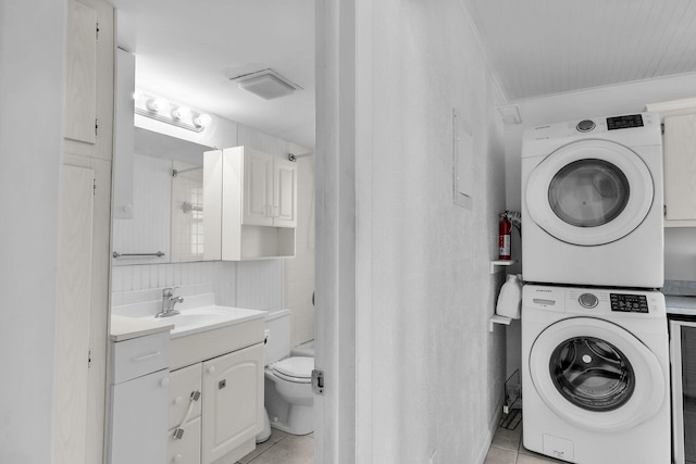 laundry area featuring laundry area, light tile patterned floors, stacked washer / drying machine, and a sink