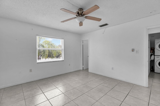 unfurnished room with light tile patterned floors, a ceiling fan, visible vents, stacked washer / drying machine, and a textured ceiling
