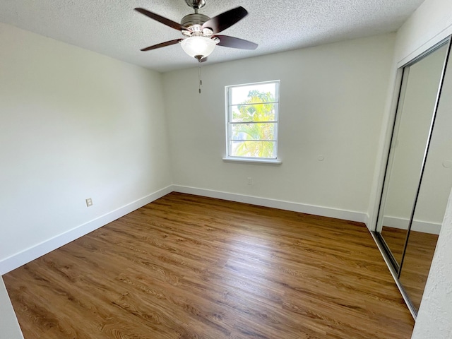 unfurnished bedroom featuring wood-type flooring, ceiling fan, a textured ceiling, and a closet